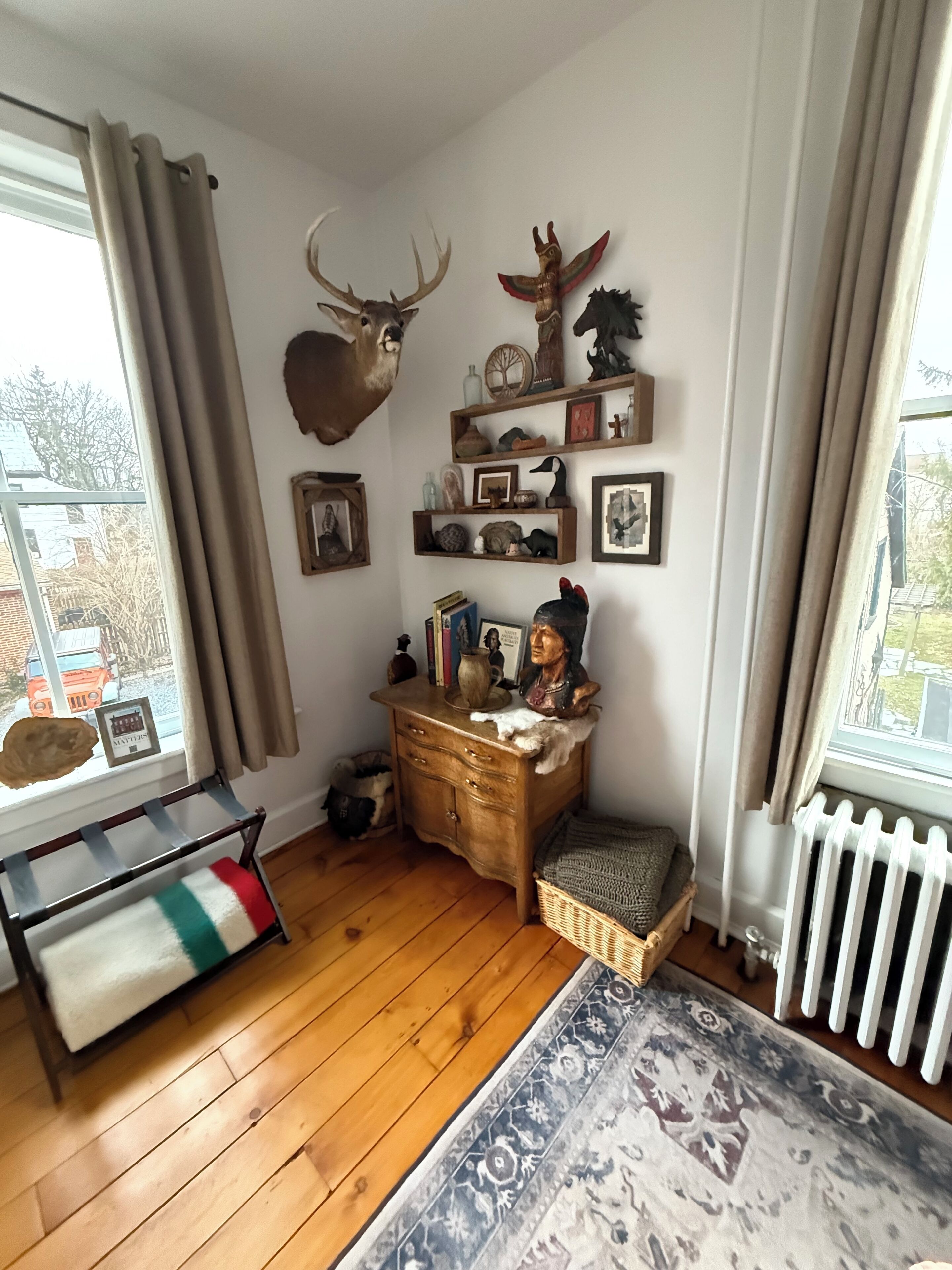 A cozy room with a wooden floor, a bench, a dresser with various items, a rug, and a window with curtains.