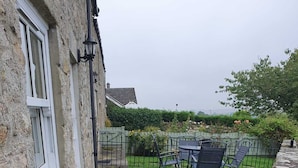 A stone house with a gated entrance, a lawn with outdoor furniture, and a clear view of the surrounding garden. - Lonin Cottage. Unwind in our cozy cottage, surrounded by scenic walks. (Barnard Castle)