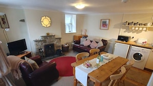 A cozy living room with a fireplace, a sofa, a television, and a dining area with a table and chairs. - Lonin Cottage. Unwind in our cozy cottage, surrounded by scenic walks. (Barnard Castle)
