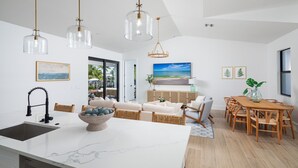 A modern kitchen with a marble countertop, a dining area with wooden furniture, and a living room with a sofa and chairs.