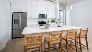 A modern kitchen with white cabinets, stainless steel appliances, a large island with bar stools, and pendant lighting.