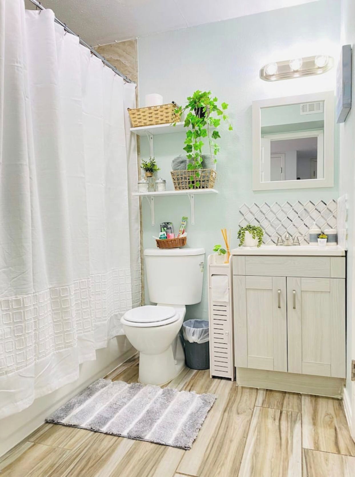 A bathroom with a toilet, a sink, a mirror, a shower curtain, and a small plant on a shelf.