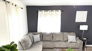 Ein modernes Wohnzimmer mit einem grauen Ecksofa, einem runden Couchtisch aus Holz und einer Topfpflanze.