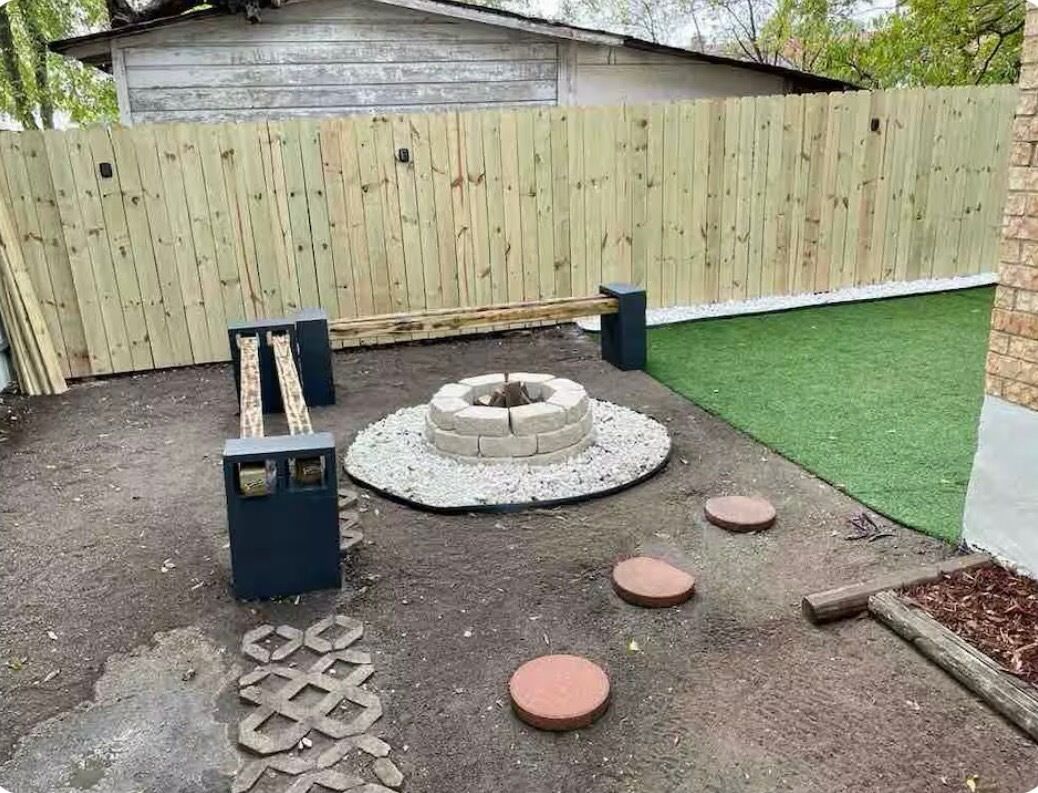 Un jardin avec une clôture en bois, un foyer circulaire et des pas japonais.