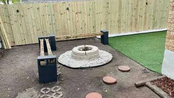 Un jardin avec une clôture en bois, un foyer circulaire et des pas japonais.