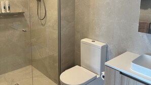 Un bagno moderno con cabina doccia in vetro, un water bianco e un mobile vanitario in legno con lavandino.