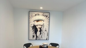 Zona pranzo con un tavolo rotondo in legno, quattro sedie nere e un grande quadro astratto appeso alla parete.
