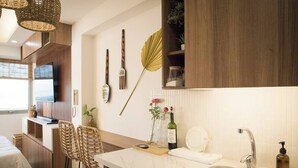 A modern kitchen with a marble countertop, a built-in sink, and bar stools. There are decorative items on the wall, including a fan and a bottle of wine.