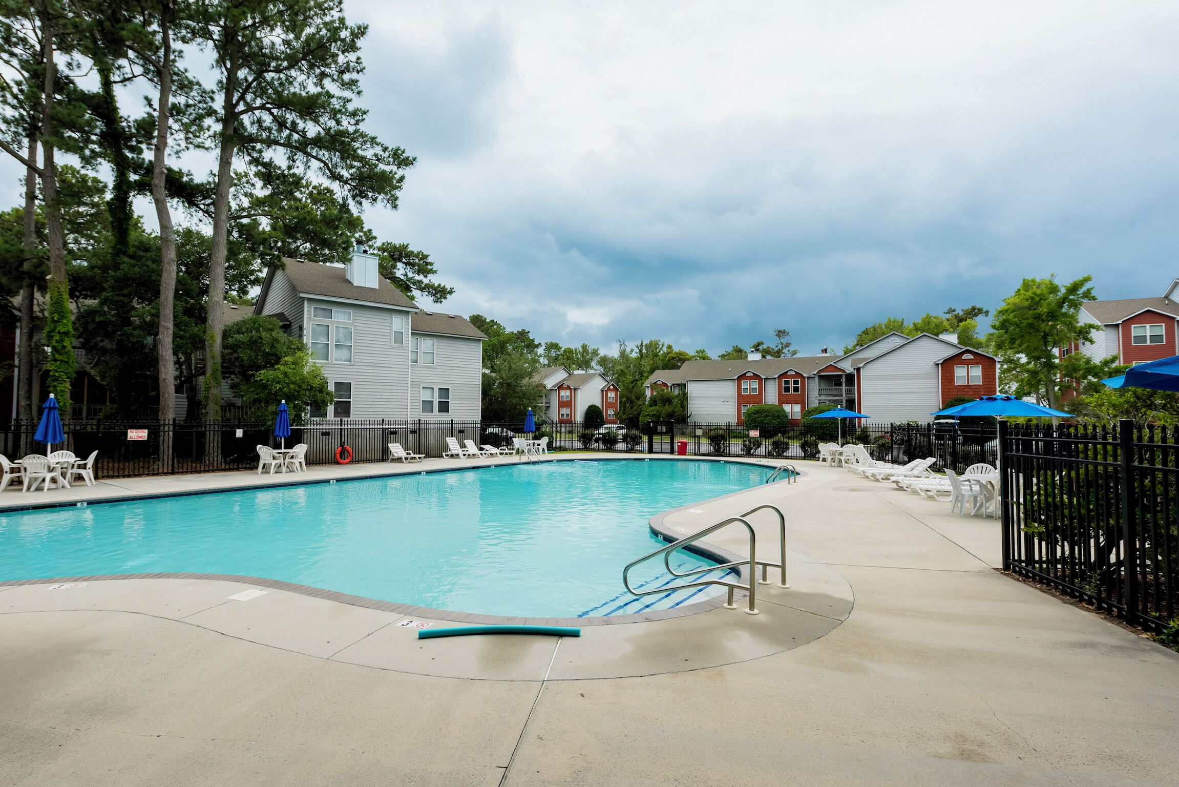 Piscina com espreguiçadeiras e guarda-sóis, cercada por edifícios residenciais.