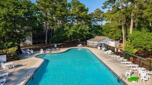 Une piscine avec des chaises longues et un petit bâtiment, le tout entouré d’arbres.