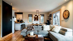 A modern living room with a sectional sofa, a coffee table, and a dining area with a kitchen in the background. - YOMI Chalet - a peaceful oasis in the heart of nature (Lac-Supérieur)
