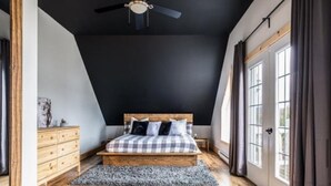 A bedroom with a wooden floor, a bed with a checkered bedspread, a ceiling fan, and a window with curtains. - YOMI Chalet - a peaceful oasis in the heart of nature (Lac-Supérieur)