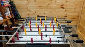 A foosball table with a wooden base and a shelf with board games in the background. - YOMI Chalet - a peaceful oasis in the heart of nature (Lac-Supérieur)