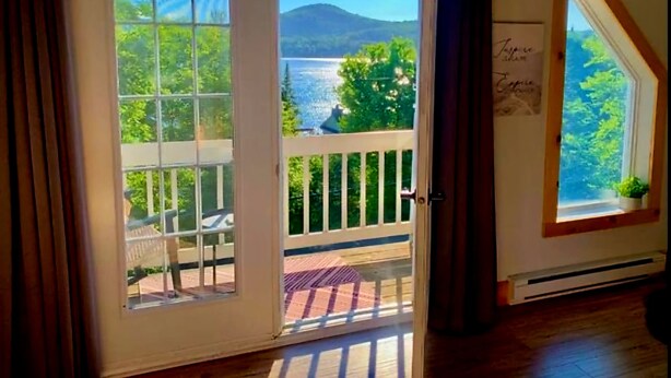 A room with a large sliding glass door leading to a balcony with a view of a lake and mountains. - YOMI Chalet - a peaceful oasis in the heart of nature (Lac-Supérieur)