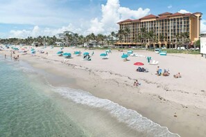 Ein Strand mit klarem Wasser, Sonnenschirmen und einem Hotel im Hintergrund.