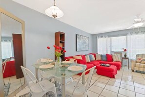 Uma sala de estar moderna com mesa de jantar de vidro, sofá vermelho e um espelho grande.