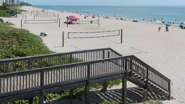 Ein Strand mit Volleyballnetz, einer Holztreppe und Strandsonnenschirmen.