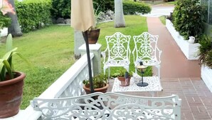 A white wrought iron bench with a table and chairs, surrounded by potted plants and a brick pathway. - BEACH OASIS - Walk 2 Beaches, Restaurants & Shops... Pets ok (Deerfield Beach)