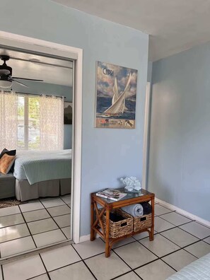 A room with a bed, a small table with a magazine, a wicker basket, and a poster on the wall. - BEACH OASIS - Walk 2 Beaches, Restaurants & Shops... Pets ok (Deerfield Beach)