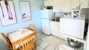 A compact kitchen with white cabinets, a refrigerator, and a dining table with chairs. - BEACH OASIS - Walk 2 Beaches, Restaurants & Shops... Pets ok (Deerfield Beach)