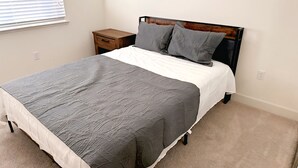 Een slaapkamer met een bed, een nachtkastje, een raam met jaloezieën en een vloerbedekking.