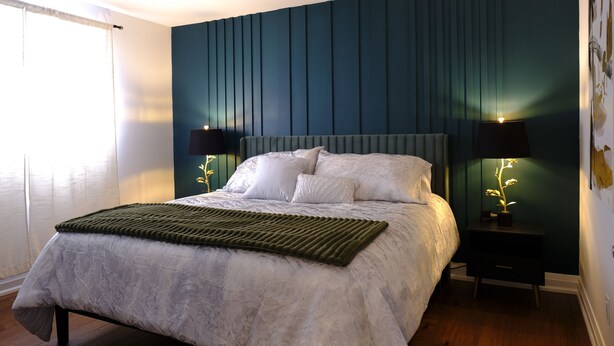 A bedroom with a bed, two bedside tables with lamps, a green rug, and a window with curtains.
