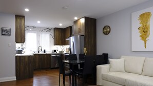 A modern kitchen with dark wood cabinets, a stainless steel refrigerator, and a dining area with a white sofa and a round coffee table.