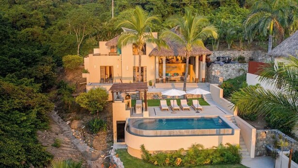 Eine moderne Villa mit Pool, Sitzgelegenheiten im Freien und einem Gebäude mit Strohdach.