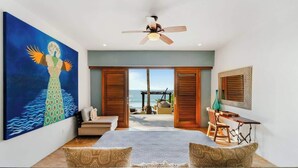 Ein Schlafzimmer mit großem Gemälde, Deckenventilator, Bett, Schreibtisch und Blick auf den Strand.