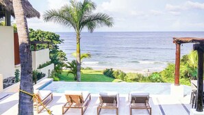 Ein Poolbereich mit Liegestühlen, einer Palme und Blick auf das Meer.