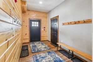 A hallway with wooden walls, a black door, a bench, and a coat rack.