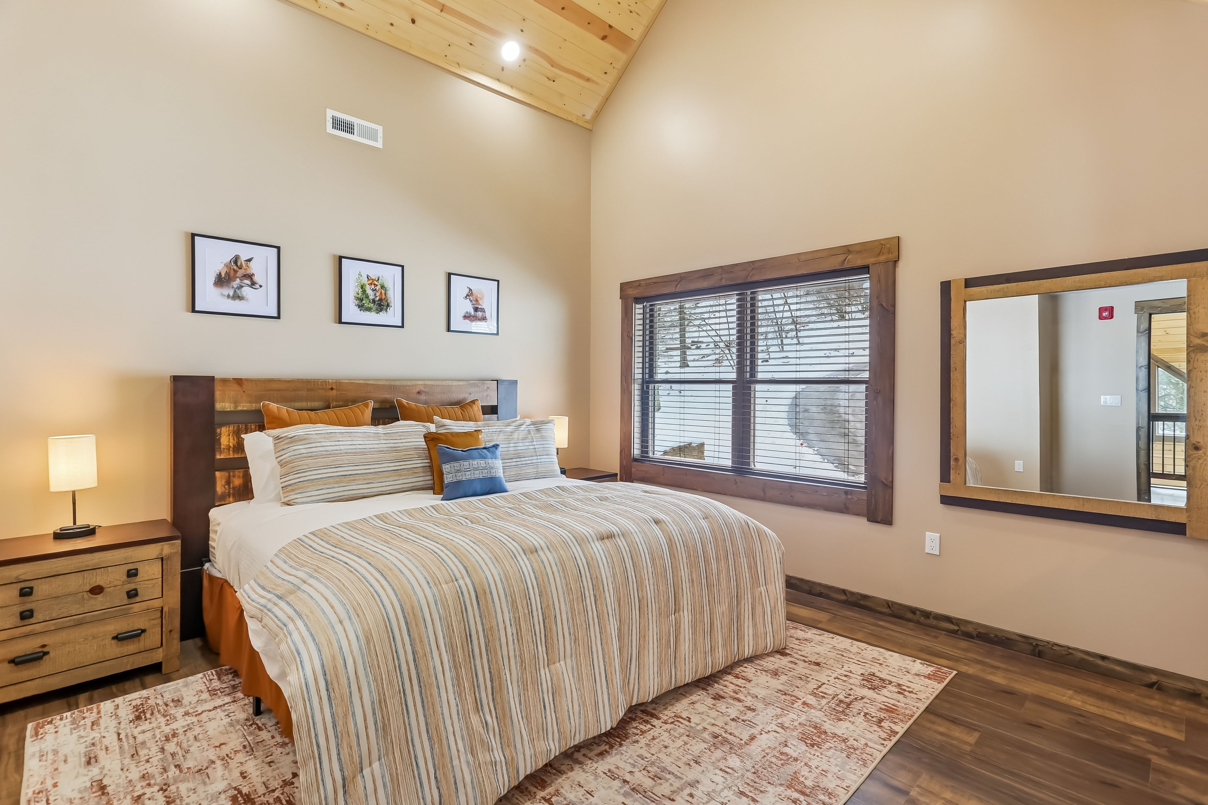 A bedroom with a bed, a nightstand, a dresser, a window with blinds, and three framed pictures on the wall.