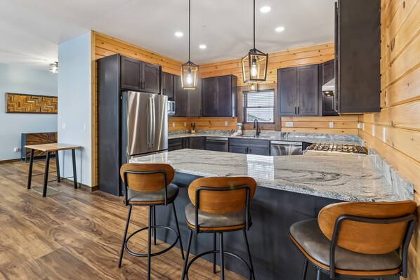 A modern kitchen with dark cabinets, stainless steel appliances, a marble island, and bar stools.