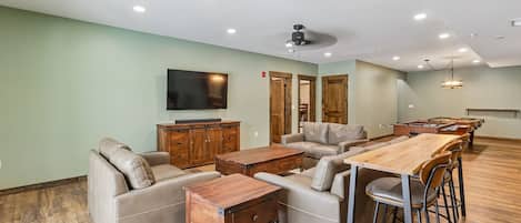 Una sala de estar moderna con televisor de pantalla plana, sofás de cuero, mesa de centro de madera y una zona de bar con taburetes.