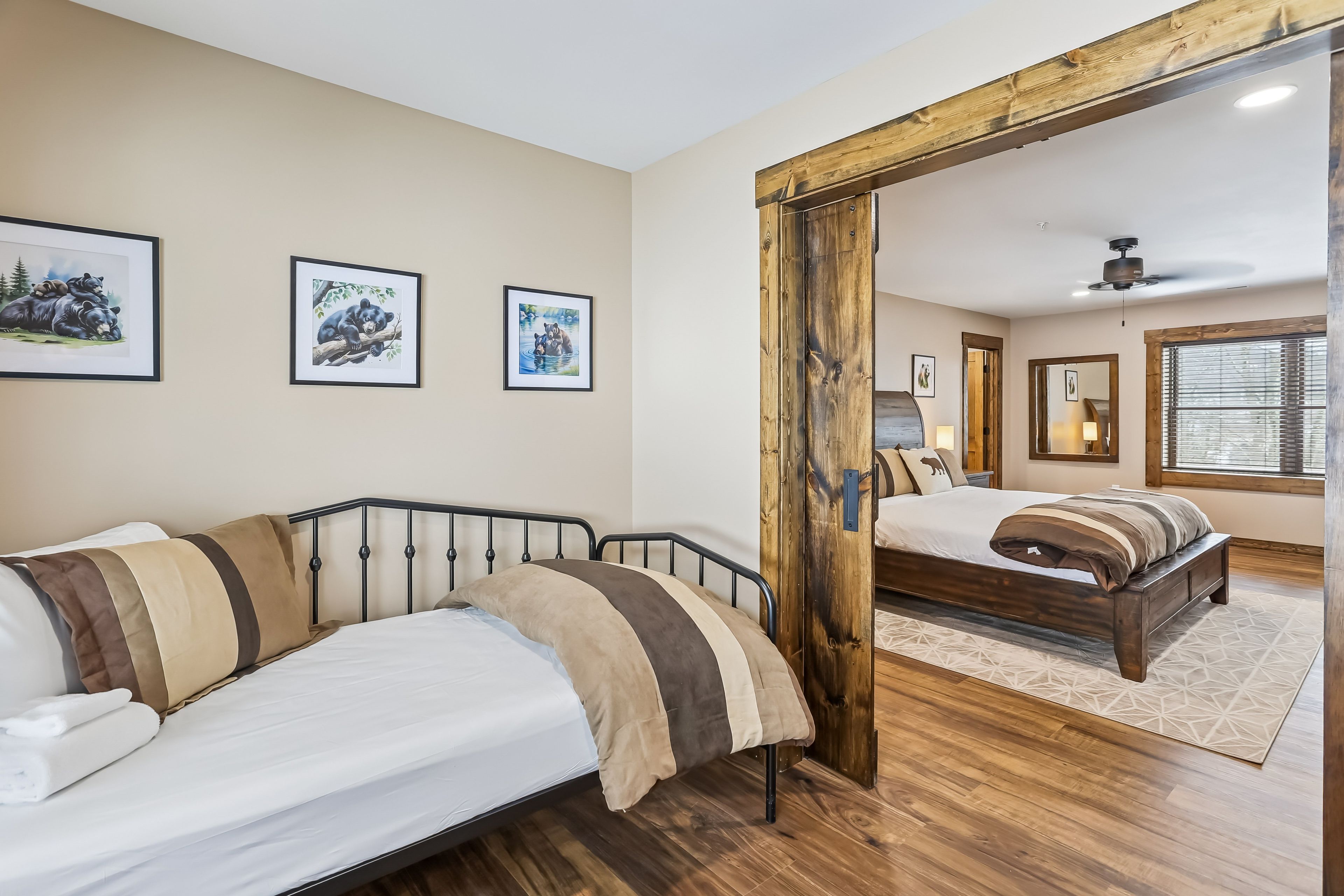 Een slaapkamer met een bed, een slaapbank, een houten vloer en een grote spiegel die een andere kamer weerspiegelt.