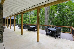 Une terrasse extérieure avec des tables et des chaises en bois, un espace couvert avec un toit en métal, et une vue sur une zone boisée.