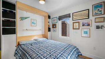 A bedroom with a bed, a wardrobe, and various framed pictures on the wall.