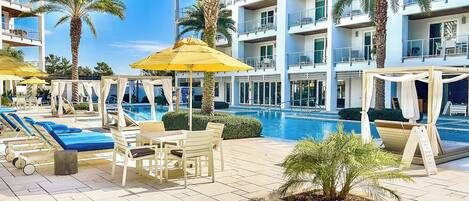 A hotel pool area with sun loungers, umbrellas, and palm trees.