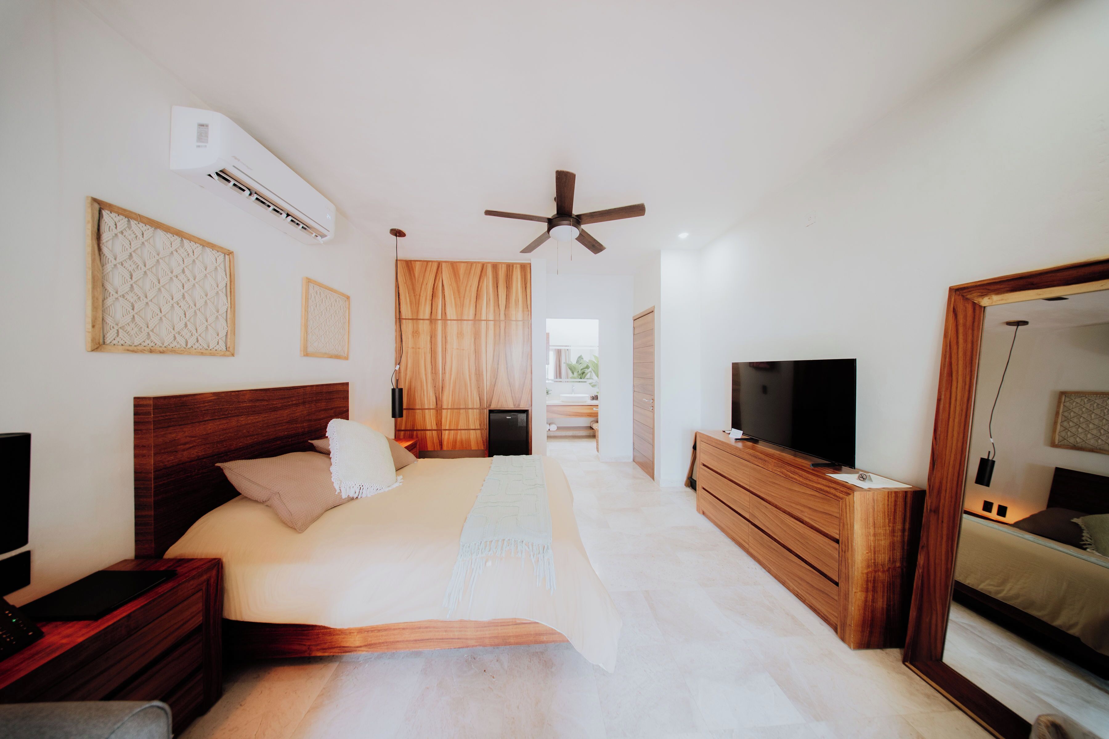 A bedroom with a bed, bedside tables, a TV, a ceiling fan, and an air conditioning unit.