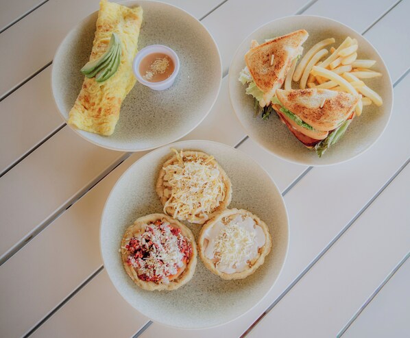 Una mesa con tres platos de comida: una tortilla de aguacate, un sándwich con papas fritas y dos tartas pequeñas de queso.