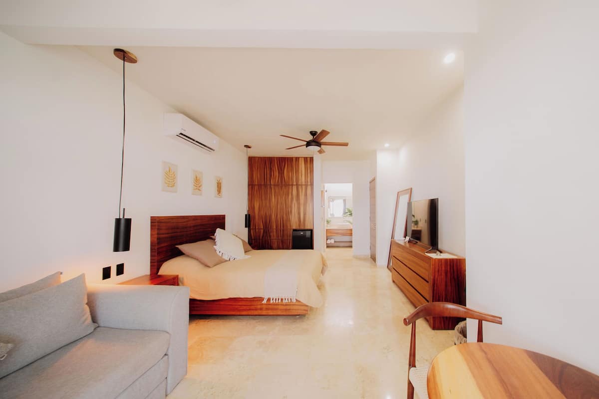 Une chambre moderne avec un lit, un canapé, une commode en bois et un ventilateur de plafond.