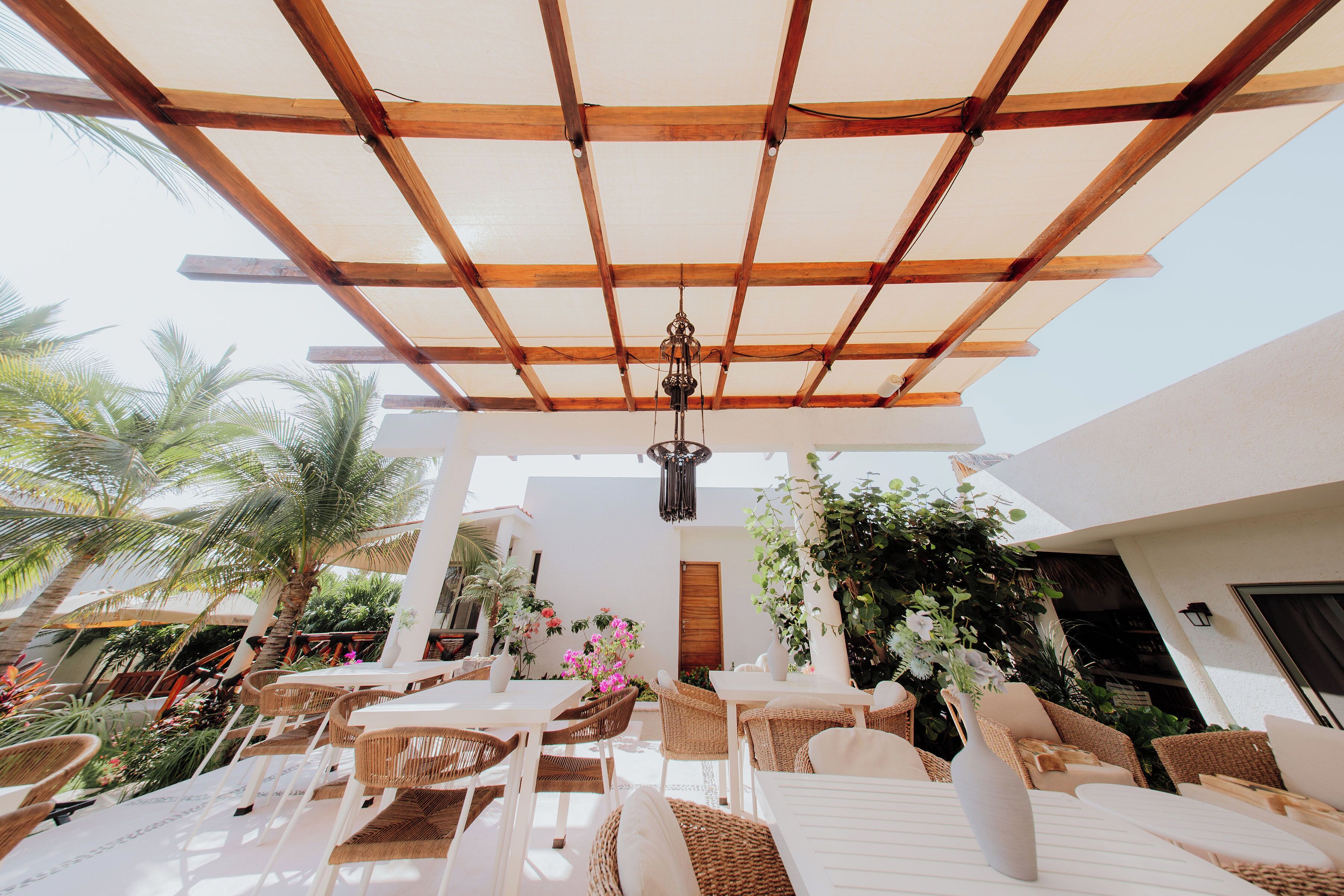 Un patio al aire libre con pérgola de madera, mobiliario de mimbre y plantas en macetas.
