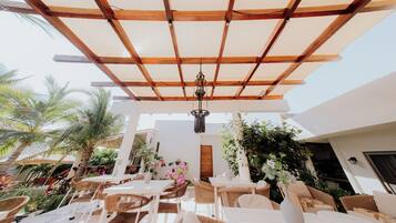Un patio al aire libre con pérgola de madera, mobiliario de mimbre y plantas en macetas.