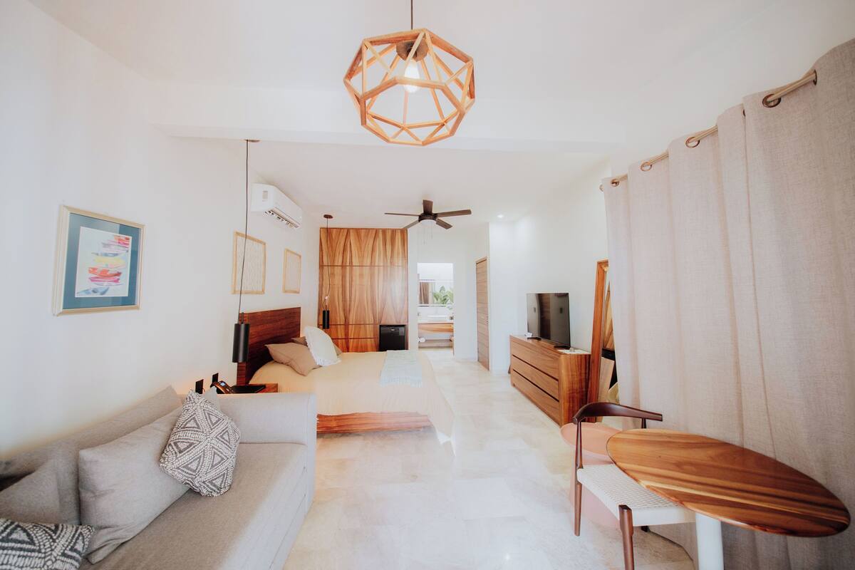 Une chambre d’hôtel moderne équipée d’un canapé, d’une table à manger en bois, d’un ventilateur de plafond et d’un téléviseur.