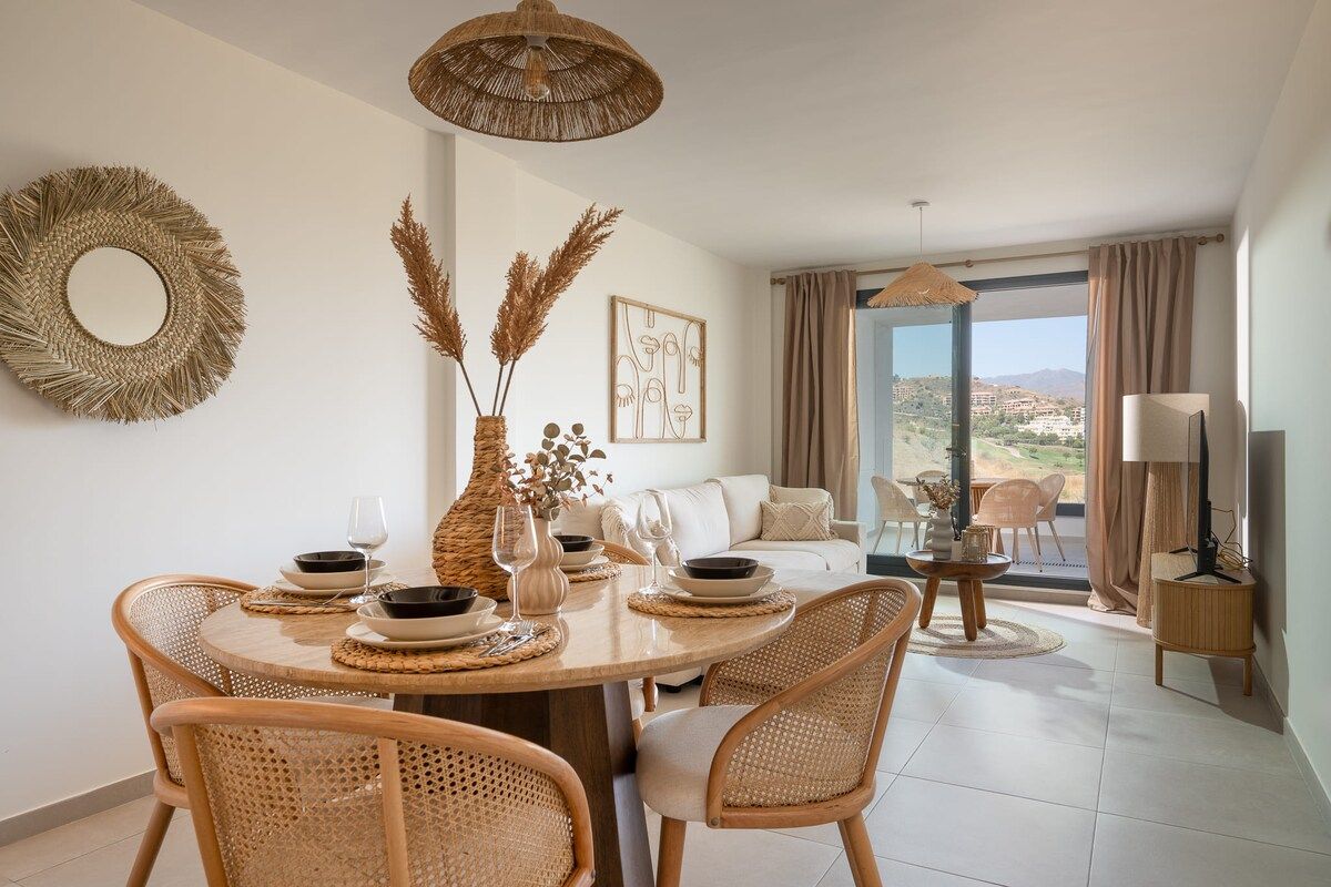 A dining area with a round table, wicker chairs, and a view through a glass door to the outside.