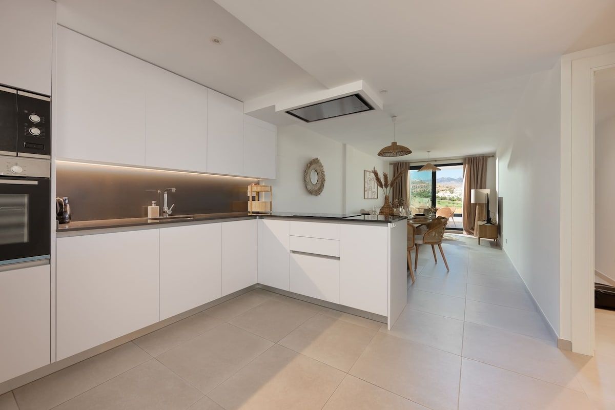 A modern kitchen with white cabinetry, a built-in oven, and a dining area with a table and chairs.