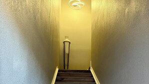 A staircase with dark wooden steps and a white base, leading to a room with a light-colored wall and a modern light fixture.
