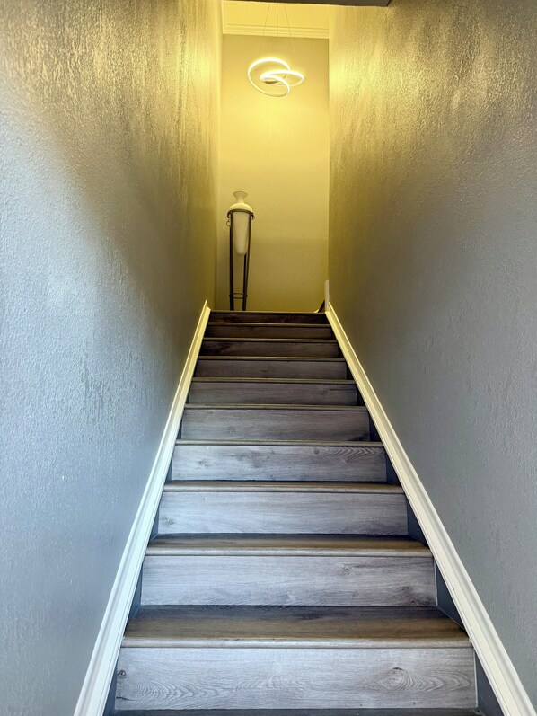 A staircase with dark wooden steps and a white base, leading to a room with a light-colored wall and a modern light fixture.