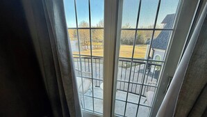 A view through a glass door with a metal railing, leading to a covered outdoor area with a stone floor and a view of a residential area.