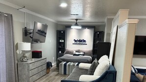 A modern living room with a dark blue sofa, a flat-screen TV mounted on the wall, and a decorative wall piece.